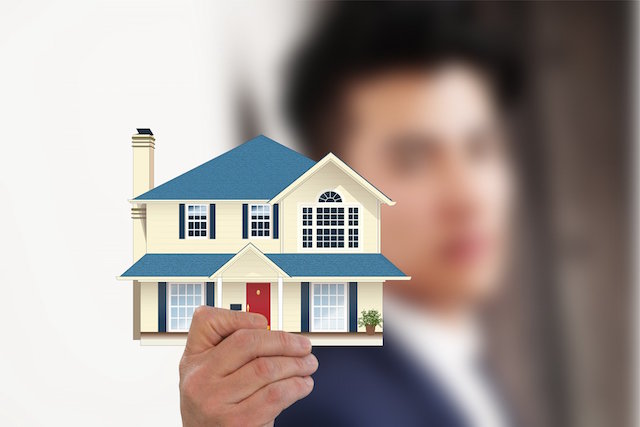 Immobilienmakler hält Hausmodell in Hand